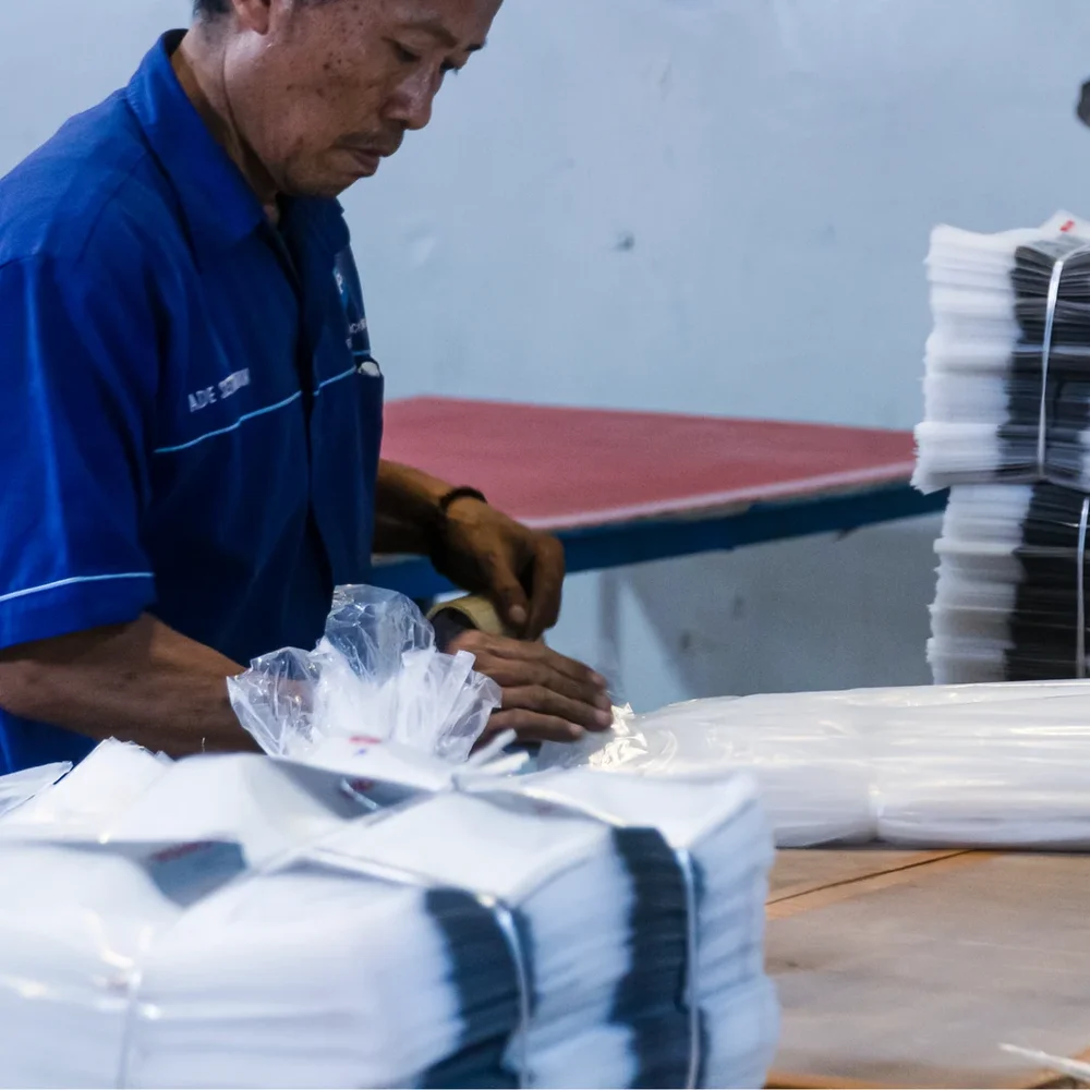 Operator JMP mengikat bundel polybag yang siap kirim — jumlah yang diikat mengikuti jadwal kirim pelanggan, bukan isi gudang.