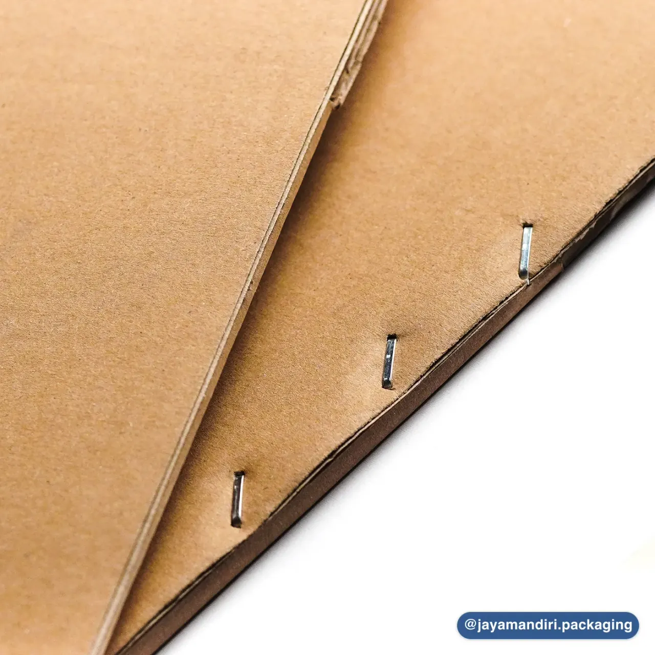 Detail sambungan jahit kawat pada karton box JMP. Kawat logam menyatukan sisi box.