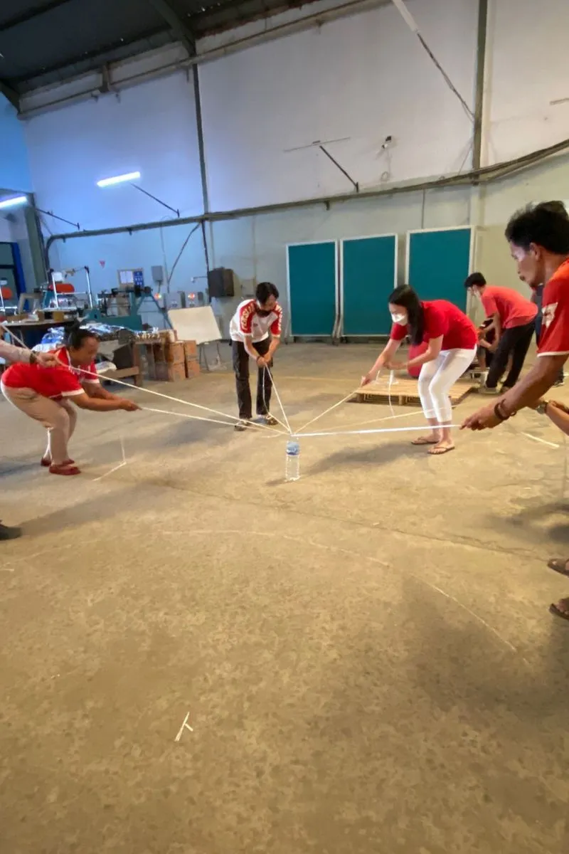 A team game moving a water bottle with ropes pulled together — six people holding tension on a single knot in the middle.