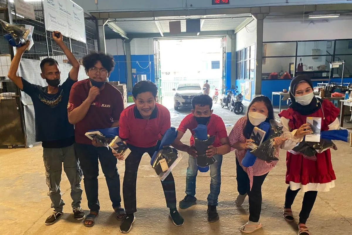 Staff in red showing off the prizes they have just won, in front of the production entrance.