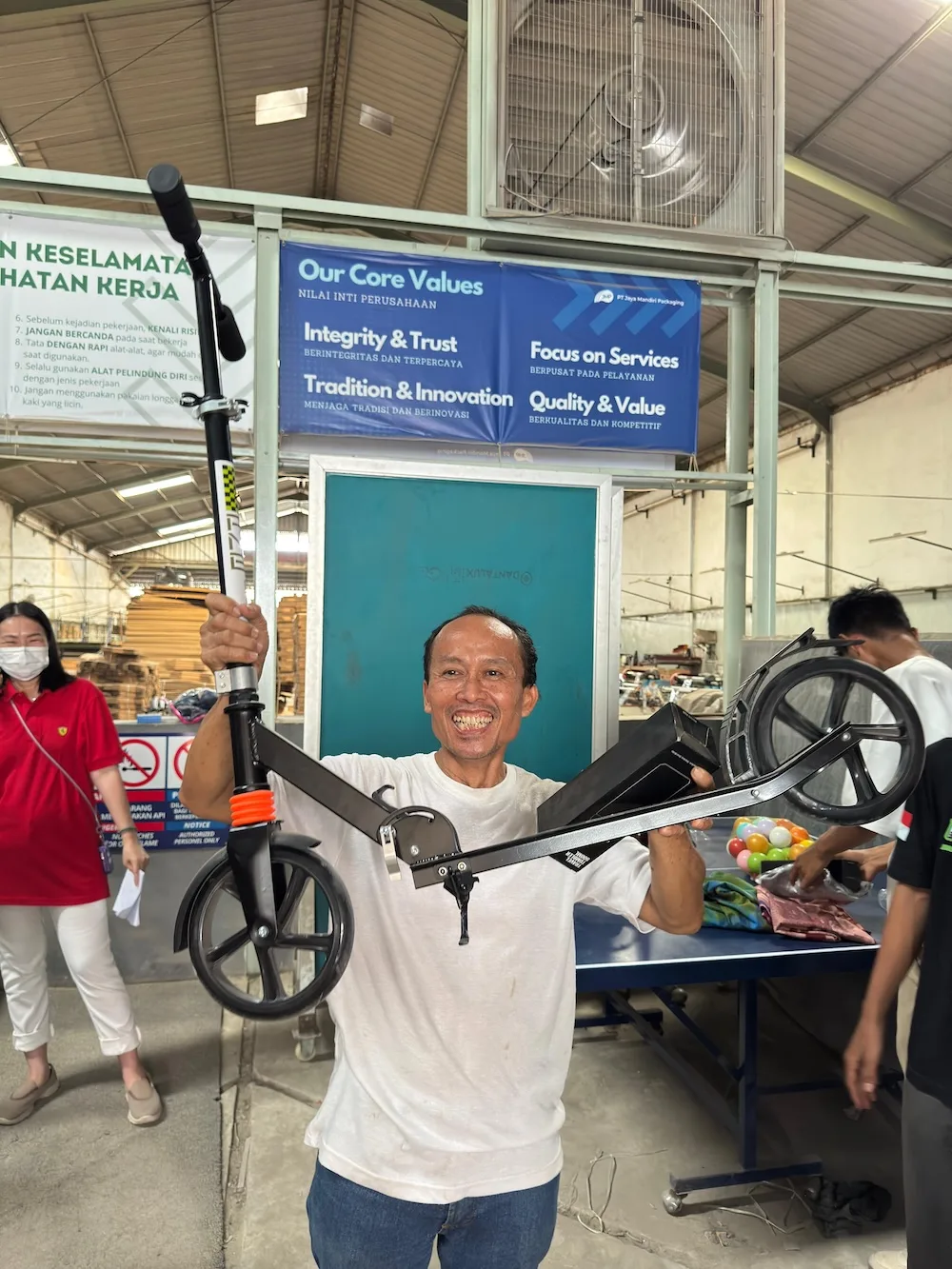 Ade Setiawan mengangkat skuter lipat yang ia menangkan sebagai doorprize, di depan banner Nilai Inti Perusahaan.