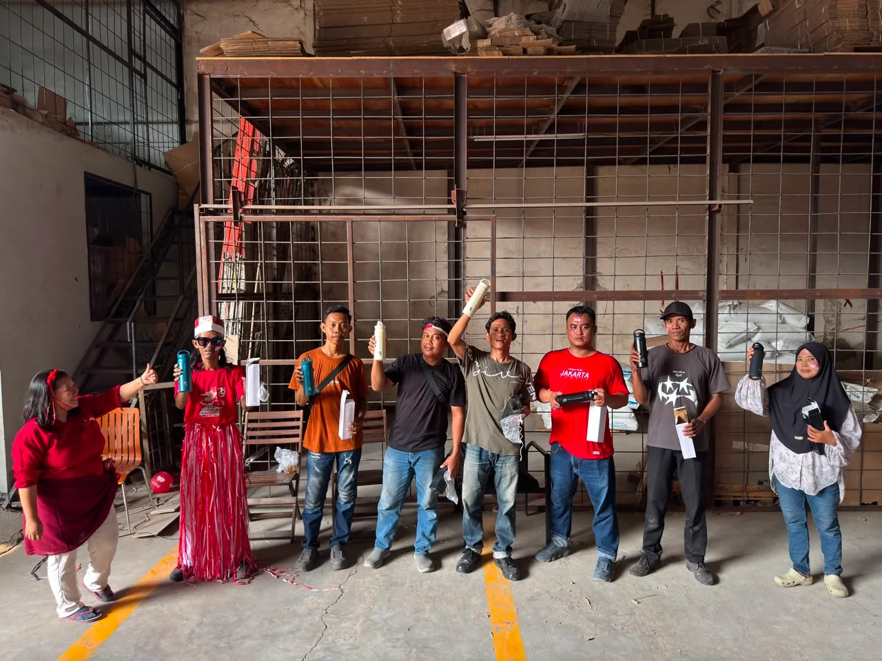 Juara 1 lomba angkat kaleng berjejer mengangkat tumbler hadiah masing-masing di depan pagar kawat gudang.