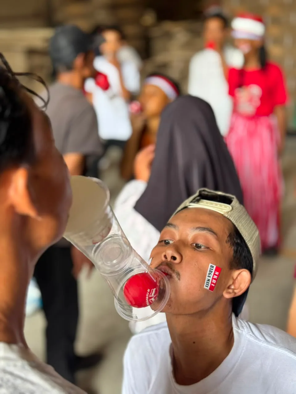 Dua pemain berhadapan mengoper bola merah antar gelas plastik yang digigit di mulut, tanpa boleh pakai tangan.