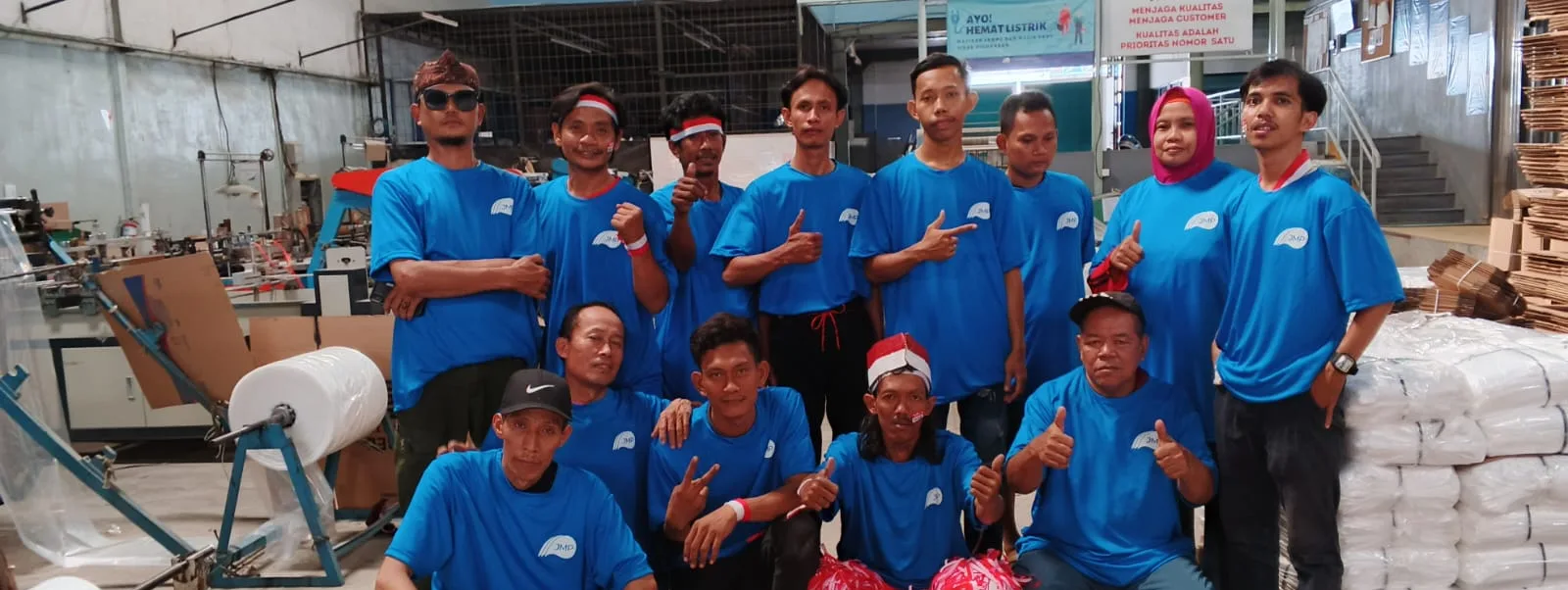 Foto bersama tim divisi polybag berkaus biru di depan mesin polybag dan gulungan film, di bawah spanduk Kualitas adalah Prioritas Nomor Satu.