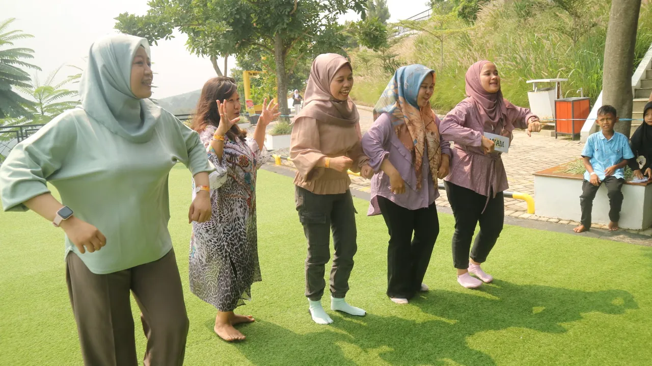 Ibu-ibu keluarga JMP kompak mengikuti games bersama di atas rumput taman.