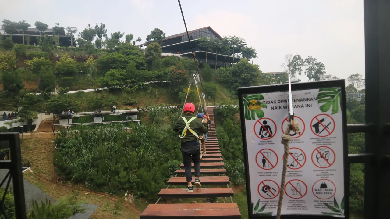 Meniti jembatan gantung dengan alat pengaman di area outbound The Nice Funtastic Park.
