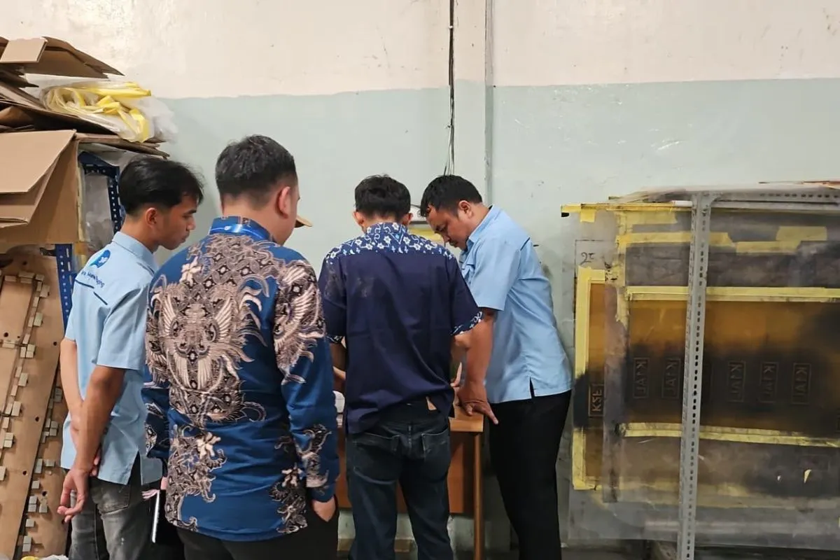 The auditor, in batik, inspecting die-cut forme storage on the JMP production floor with the team, in front of racks of labelled formes.