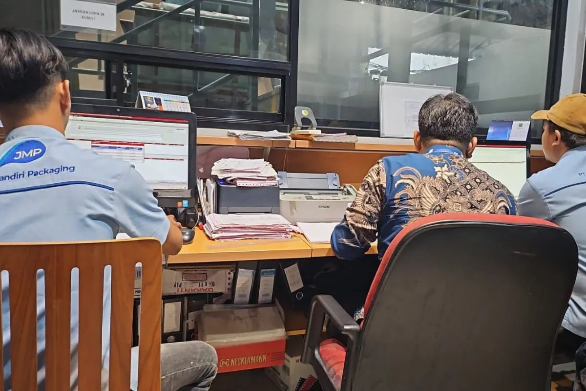 Document and quality-record review at a JMP office desk with the auditor, among stacks of files and delivery notes.