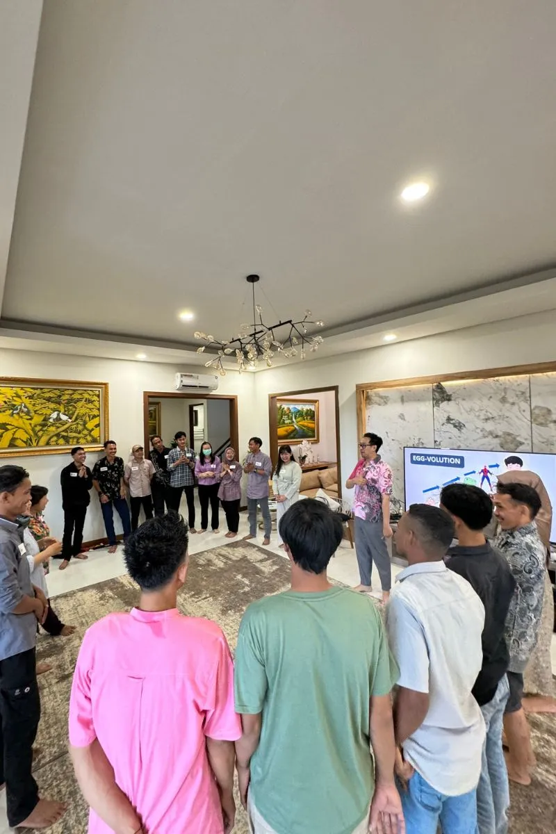 The facilitator explaining a warm-up game in front of the screen, participants standing in a circle around the room.