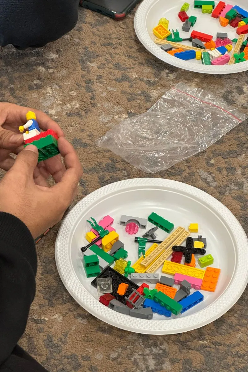 LEGO bricks handed out on white dinner plates, one participant assembling a small piece in his hands.