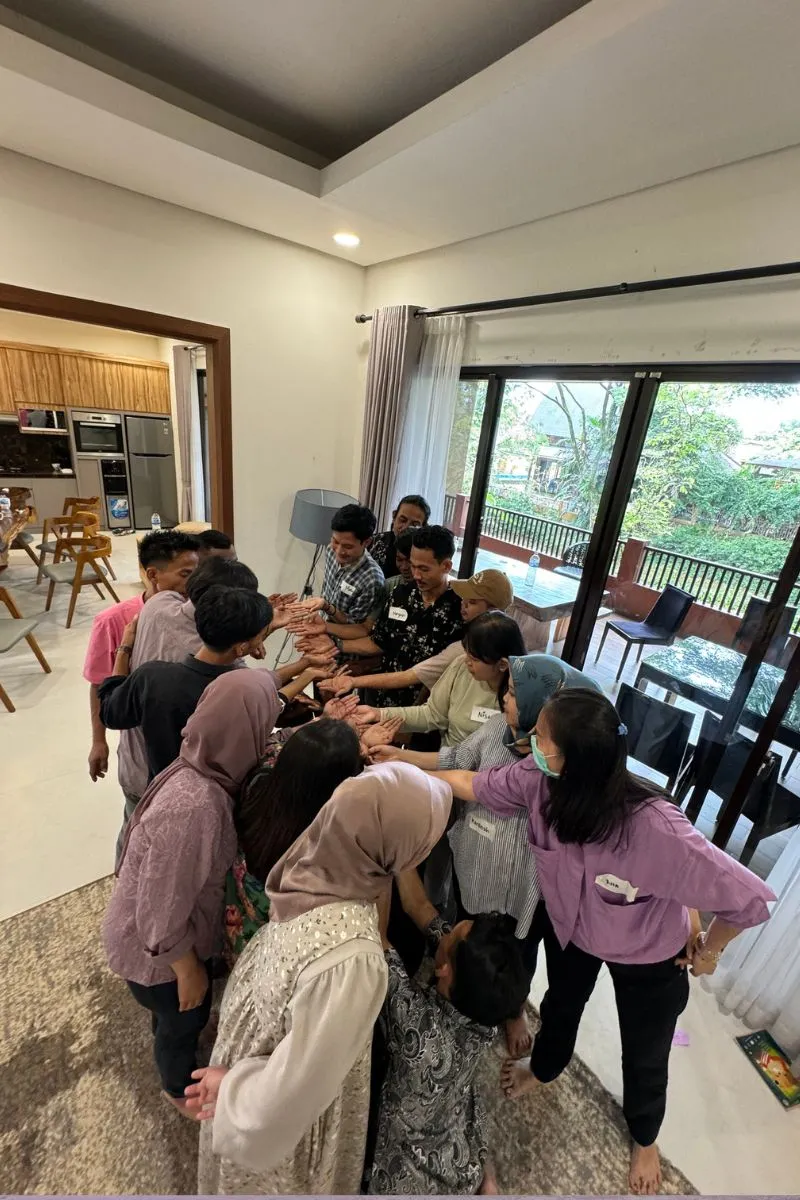 Overhead view of the team forming a tight circle with hands joined, the terrace and trees visible beyond.