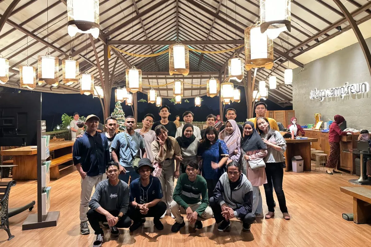 Group photo of the whole team at dinner, in a joglo-roofed restaurant lit by rattan lanterns.