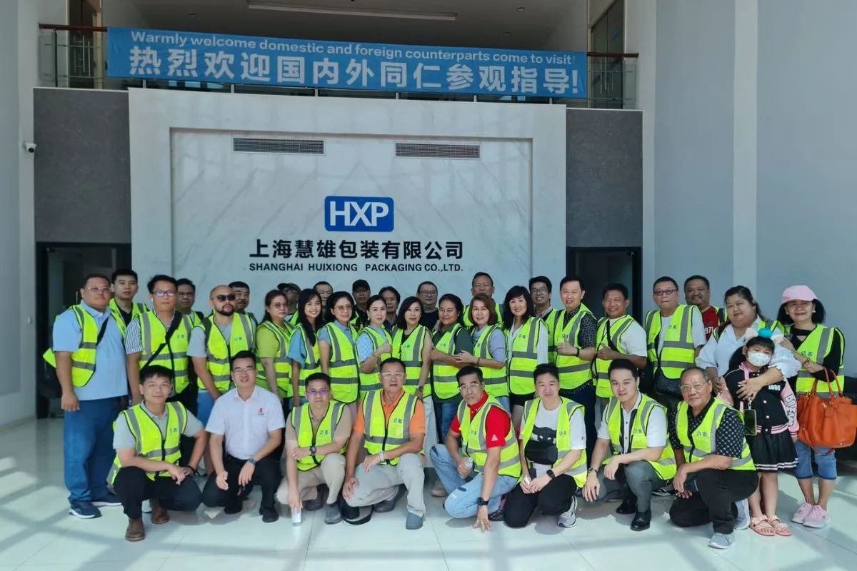 The group in hi-vis visitor vests during a plant tour at Shanghai Huixiong Packaging, under a welcome banner.