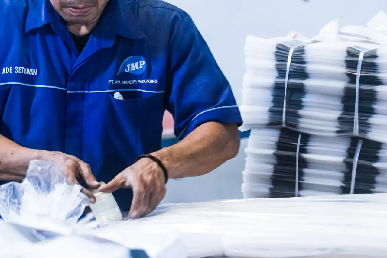 Operator JMP mengemas dan mengikat polybag PE/PP yang sudah jadi di lantai produksi.