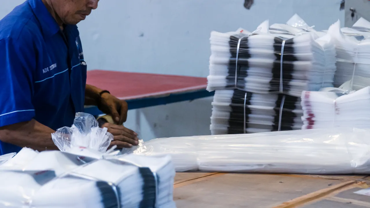 Operator JMP membundel tumpukan polybag di lantai produksi.